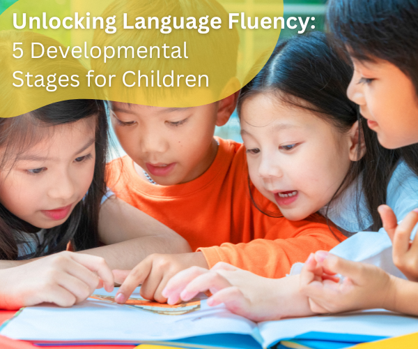 four asian children huddled together looking at an open book and pointing at a page